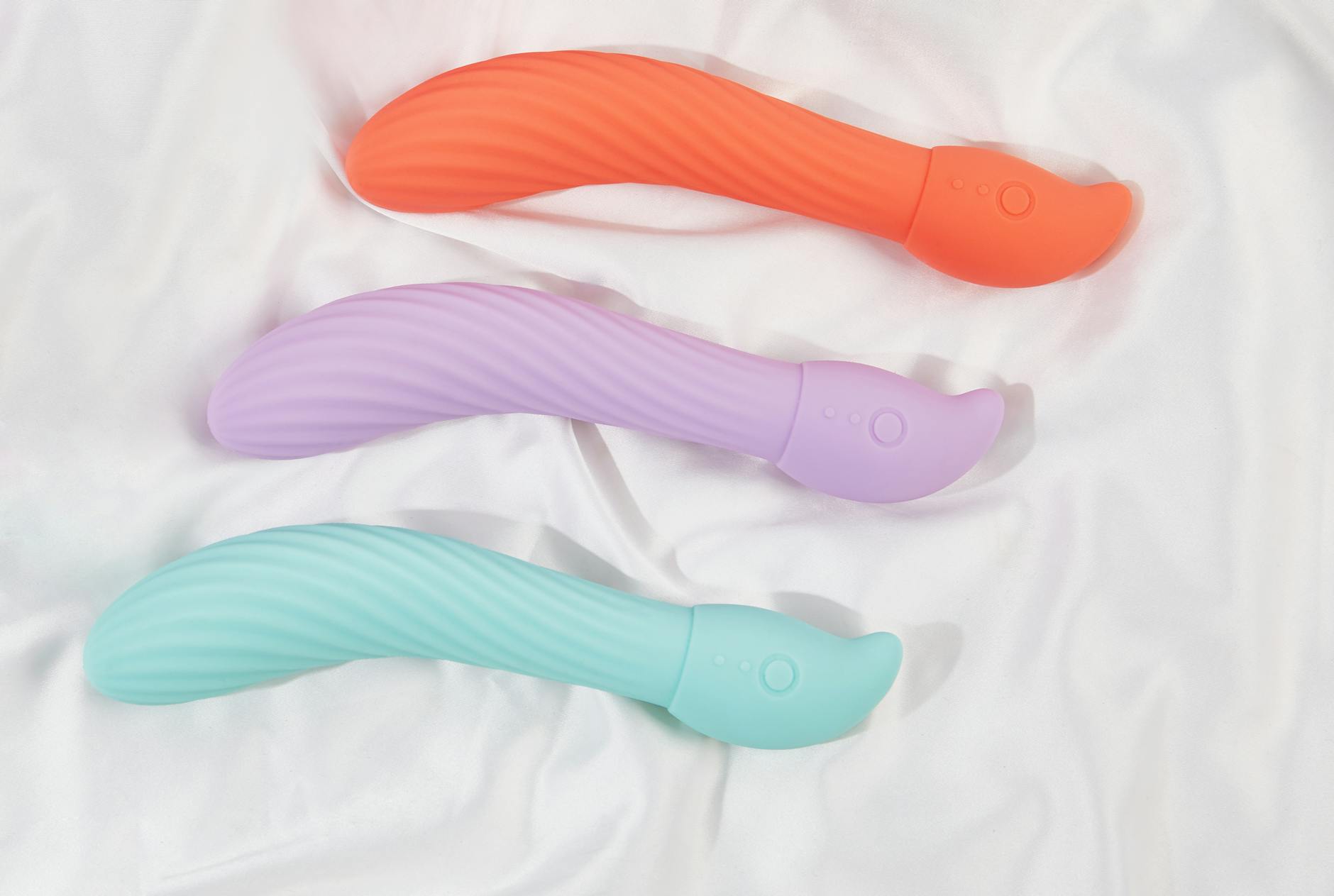 Tre vibratori colorati su tessuto bianco, evidenziando la loro texture morbida e il design ergonomico