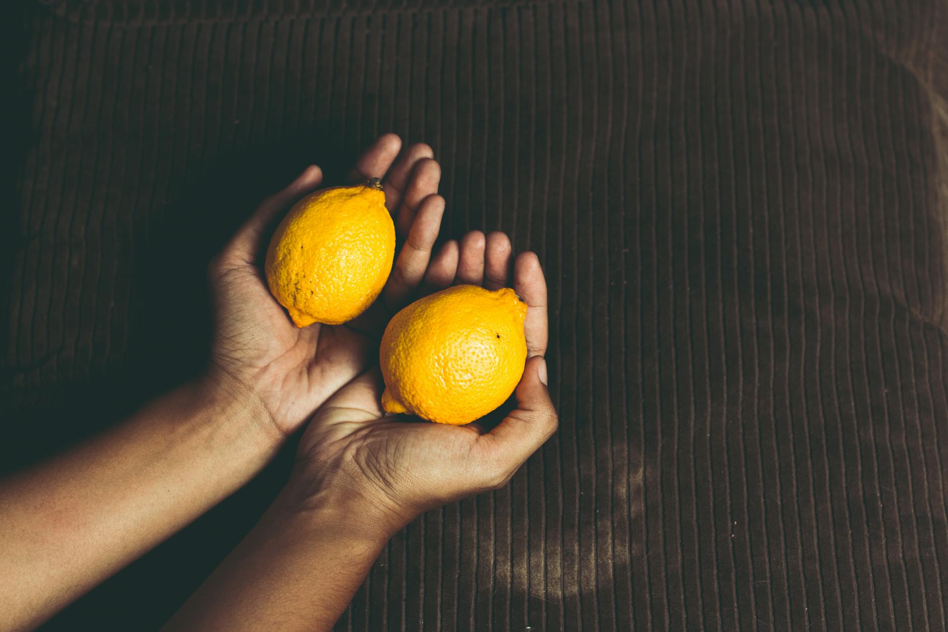Due mani che tengono limoni freschi su una superficie marrone, simbolo di freschezza e vitalità