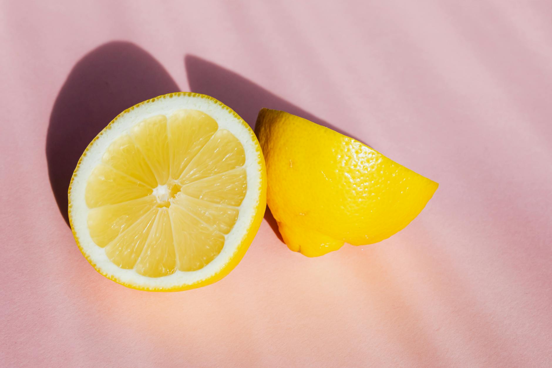Due metà di limone fresco su sfondo rosa, illuminate da raggi di sole, simboleggianti freschezza e vitalità