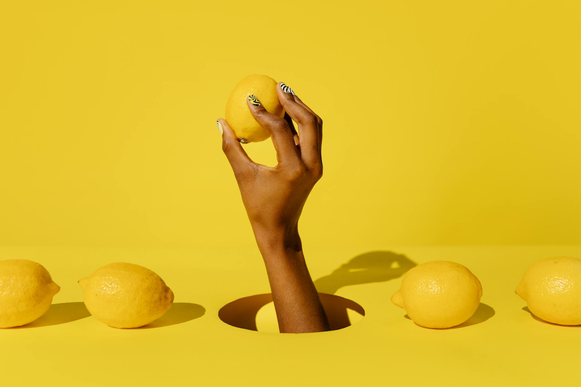 Una mano che regge un limone fresco su uno sfondo giallo vivace, rappresentando la freschezza e il ringiovanimento del piacere senza dolore