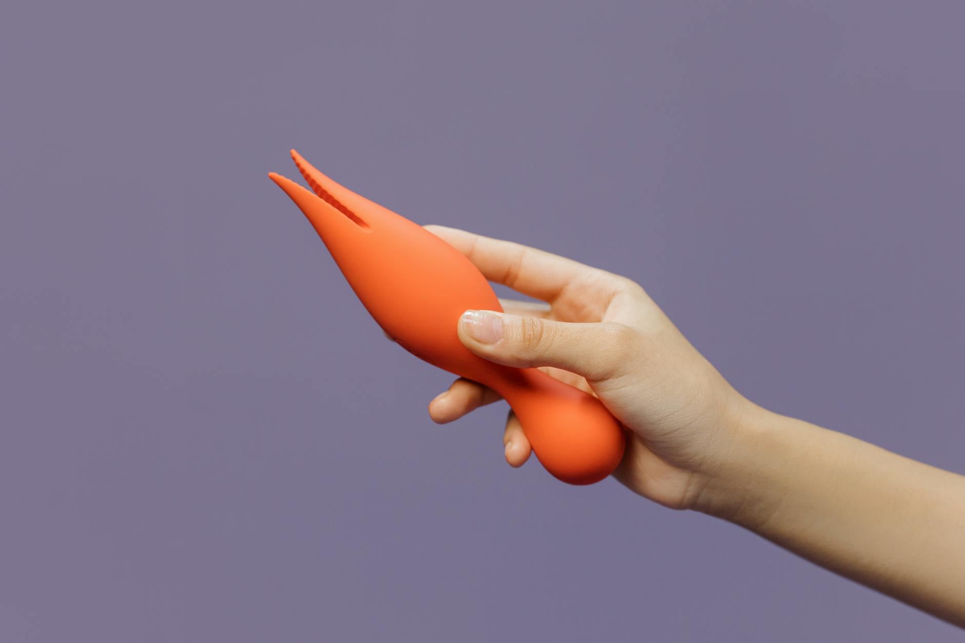 Una mano che tiene un vibratore arancione contro uno sfondo minimalista, mostrando sensualità moderna