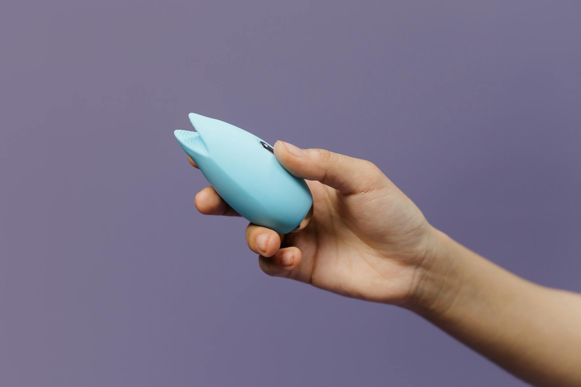 Mano con unghie bianche che regge un limone su sfondo rosa, circondata da altri limoni