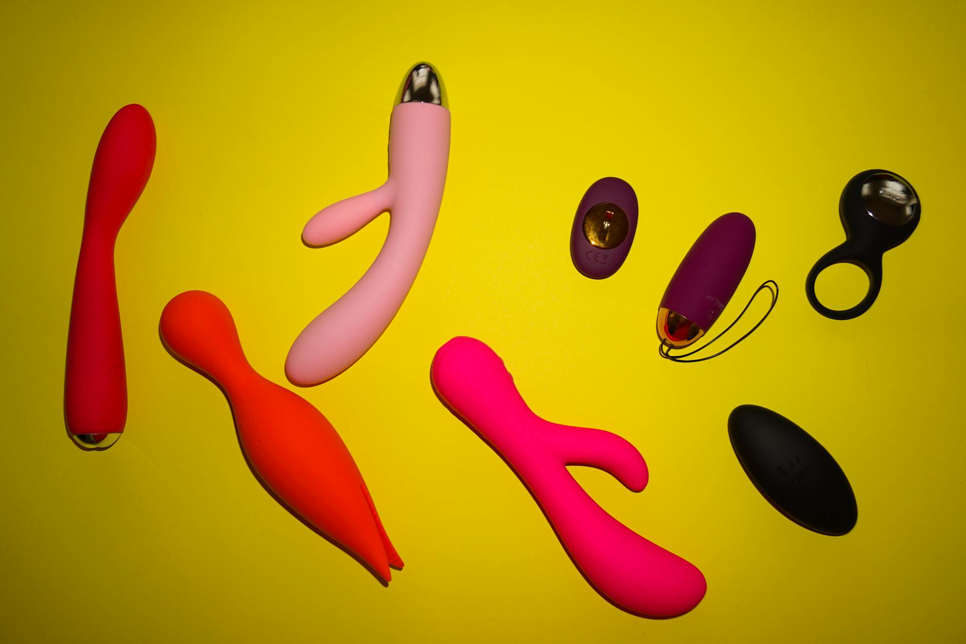 Two hands holding pink and blue silicone vibrators against a pastel background